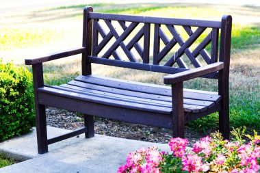 Çimento yastığında yeşil çim ve çiçeklerle plastik ahşaptan yapılmış park bankı.