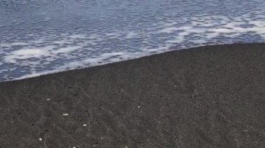 Beyaz deniz kabuğu parçalarıyla okyanus dalgası gri kumlara vuruyor.