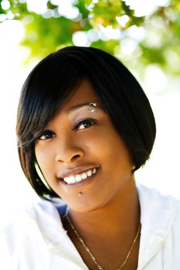 Çekici, gülümseyen, kısa saçlı, açık hava portresi çizen Afrikalı Amerikalı kadın.