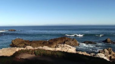 Monterey Körfezi dalgaları mavi gökyüzüyle havalanan martılarla kayalara çarpıyor.