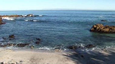 Okyanus dalgaları kumsalda kıyıya vuran kayalar ve açık mavi gökyüzü Monterey Körfezi Pasifik Korusu