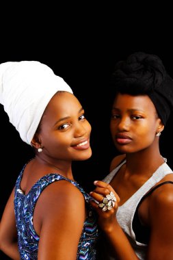 Siyah ve beyaz başlıklı iki Afro-Amerikan kadın karanlık arka planda kameraya bakıyor.