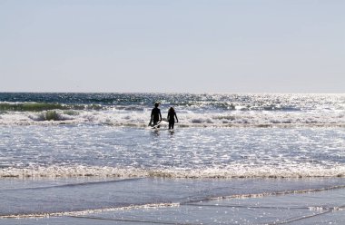 Oceanside, California, ABD - 08 Nisan 2024: Dalış elbiseleriyle denize bakan erkek ve kadın sörf tahtası