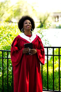 Orta yaşlı, kırmızı kilise cüppeli Amerikalı kadın elinde İncil 'le dışarı bakıyor.