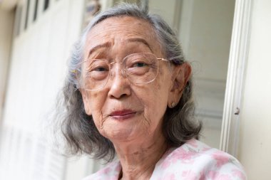 Güzel, sağlıklı Güneydoğu Asyalı, gözlüklü, gülümseyen ve kameraya bakan yaşlı bir kadın.