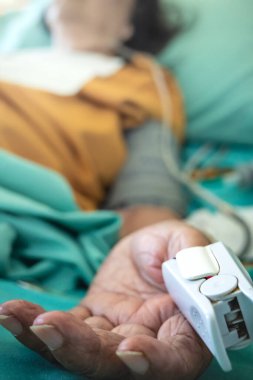 Doygunluk, nabız ve kalp atışlarını ölçmek için hastanede yatan hasta, Asyalı yaşlı kadın yatalak, oksitmetre üzerinde yatıyor.