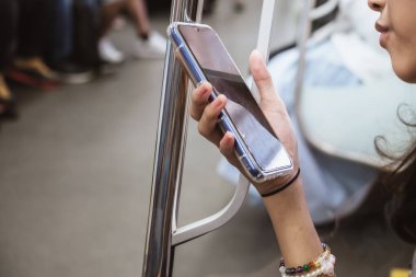 Asyalı genç kız yolcu metroda otururken akıllı telefon kullanmaktan zevk alıyor.