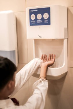 Uzun kollu gömlekli Asyalı çocuk tuvalette ellerini kurutuyor.