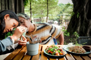 Southeast Asian father teaching his teenage daughter how to become a good foodgrapher at an outdoor restaurant clipart