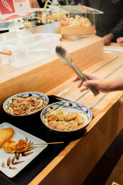 Bir Japon restoranında yemek için müşteri kuyruğu oluşturun ve tezgahtan çeşitli yemekler alın.