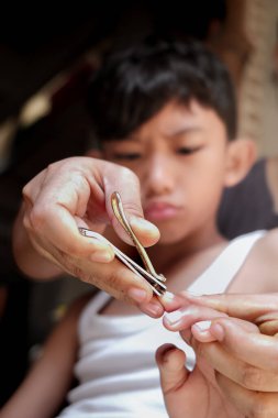 Annenin oğlunun tırnak makasıyla tırnaklarını kestiği yakın çekim görüntüsü. Çocuğun yüzündeki somurtkan ifade isteksizliğini gösteriyor..