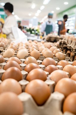 Arka planda müşteri ve personelle markette satılmak üzere karton paketlenmiş tavuk yumurtaları.