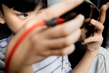 Bir arabanın içinde şarj olurken akıllı telefondan online oyun oynayan Asyalı çocuk.