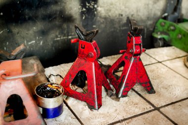 Bir çift kullanılmış ve kirli kırmızı kriko standı ve araba servisinin garajında yere bir kutu yağ.