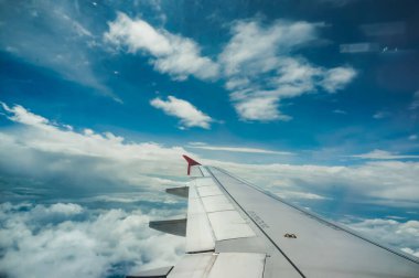 Parlak ve güzel mavi gökyüzü ve arka planında beyaz bulutlar olan uçak kanadı yolcu penceresinden görülüyor. Hava yolculuğu kavramı.