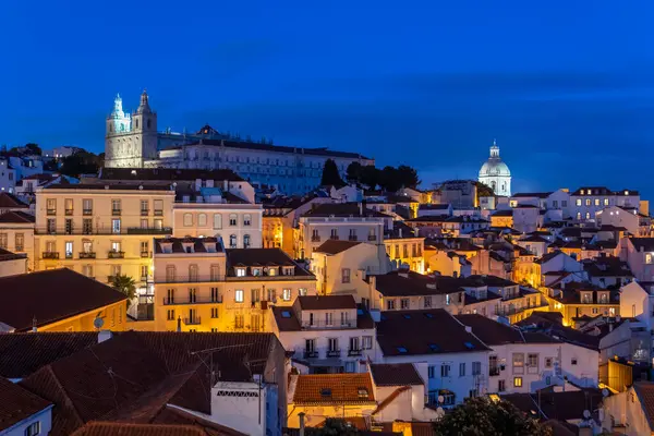 里斯本市晚上在葡萄牙 Alfama区与教堂和圣维森特德福拉修道院在山上的城市景观 免版税图库照片