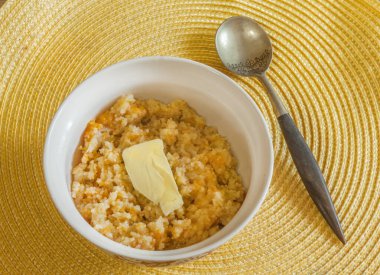 Hot rice porridge with pumpkin and butter on a yellow napkin. View from above.