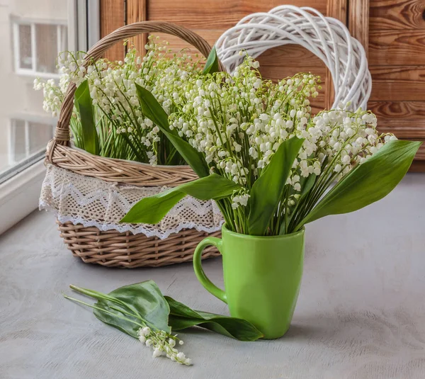 Blooming lilies of the valley or convallaria majalis  in a vintage  basket and green cup on the window. Symbol of the first of May in France \