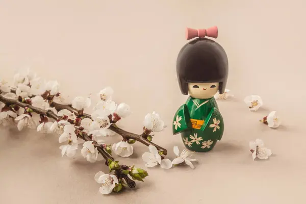 灰色の背景にある花のエプロコットの枝の隣にある日本の伝統的な人形のこだわり 大量生産された製品 バナー ポストカード カレンダー ソーシャルネットワークの背景 テキストの場所 — ストック写真