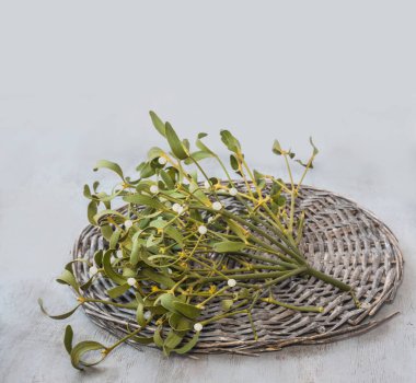 Mistletoe leaf sprig with berries on wicker circle on gray table. Preparing mistletoe branches for home decoration for Christmas. Space for text. Background for message, banner, calendar clipart