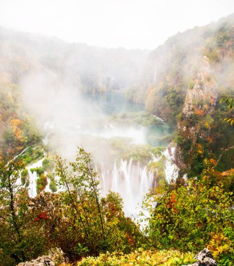 Plitvice göllerindeki yağmurlu, sisli sonbahar havasında sakin bir orman ortamında resim gibi sonbahar şelalesi.