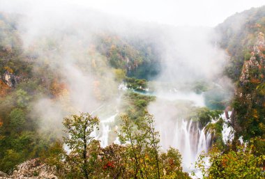 Plitvice göllerindeki yağmurlu, sisli sonbahar havasında sakin bir orman ortamında resim gibi sonbahar şelalesi.