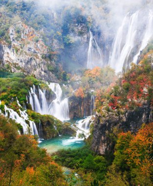 Plitvice göllerindeki yağmurlu, sisli sonbahar havasında sakin bir orman ortamında resim gibi sonbahar şelalesi.