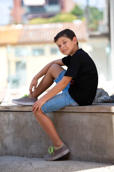 Chłopiec Spodenkach Czarny Shirt Siedzący Kamiennej Ławce Patrząc Kamerę — Zdjęcie stockowe