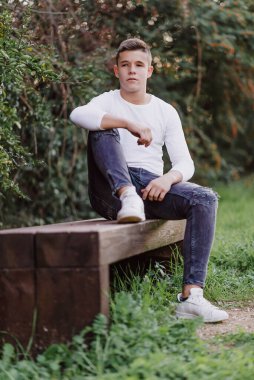 Parktaki bankta oturan genç, kameraya bakıyor.