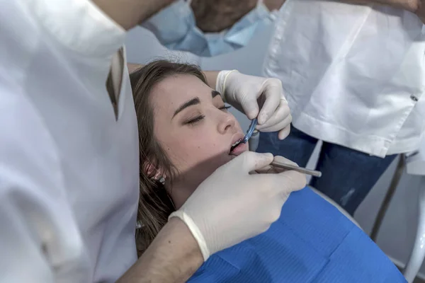 A female dentist treats a patient\'s teeth. The dentist makes a professional cleaning of the teeth of a young female patient in the dental office.