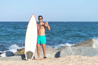 Plajda elinde sörf tahtası olan çıplak bir sörfçü.