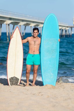 Plajda elinde sörf tahtası olan çıplak bir sörfçü.