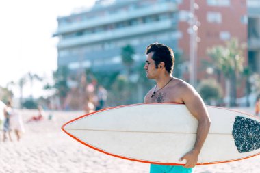 Plajda elinde sörf tahtası olan çıplak bir adam.