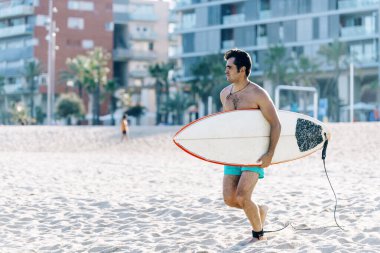 Plajda elinde sörf tahtası olan çıplak bir adam.