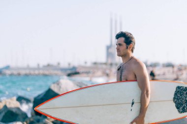 Plajda elinde sörf tahtası olan çıplak bir adam.