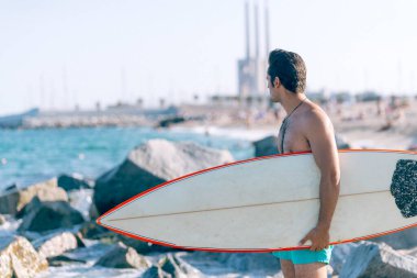 Plajda elinde sörf tahtası olan çıplak bir adam.