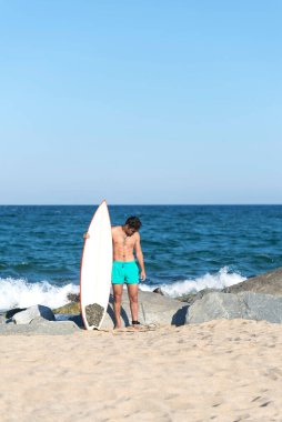 Plajda elinde sörf tahtası olan çıplak bir sörfçü.