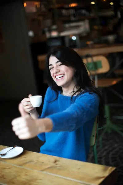 Radosna Kobieta Niebieskim Swetrze Pije Filiżankę Kawy Kawiarni Dając Kciuki Obrazek Stockowy