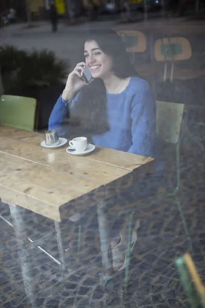 Radosna Młoda Kobieta Niebieskim Swetrze Rozmawia Przez Telefon Siedzi Sama Zdjęcie Stockowe