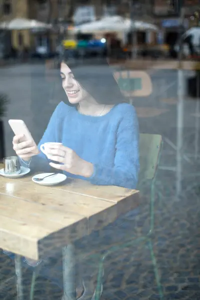 Молодая Женщина Синем Свитере Фокусируется Своем Телефоне Кафе Чашкой Кофе Стоковое Изображение