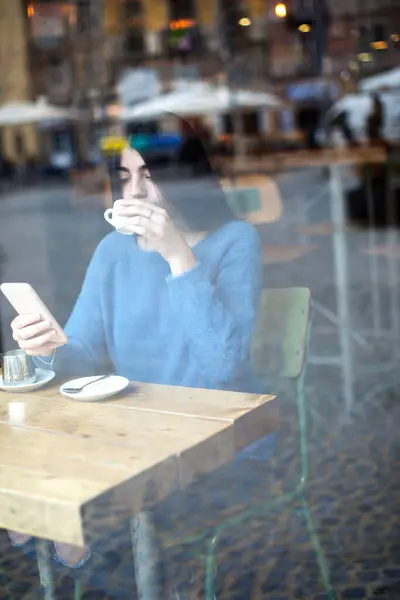 Молода Жінка Синьому Светрі Фокусується Своєму Телефоні Кафе Чашкою Кави Ліцензійні Стокові Фото