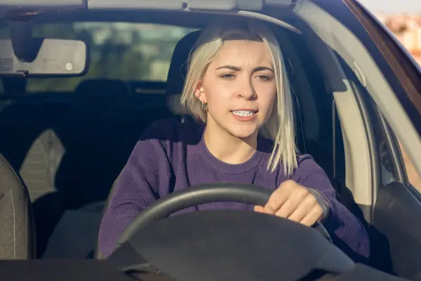 Konsentrert Ung Blond Kvinne Iført Lilla Genser Som Kjører Bil stockbilde