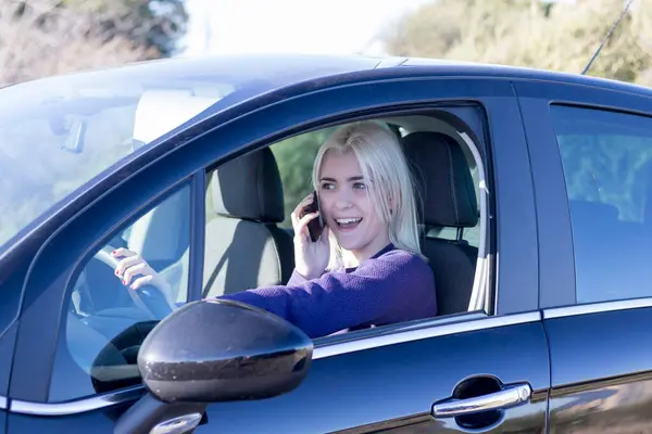 자동차의 운전석에 앉아있는 그녀의 전화에 보라색 스웨터에 금발의 로열티 프리 스톡 사진