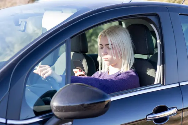자동차의 운전석에 앉아있는 그녀의 전화에 보라색 스웨터에 금발의 로열티 프리 스톡 이미지