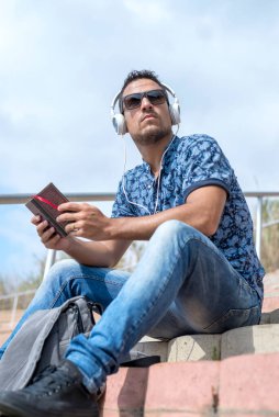 Kulaklık takmış sıradan bir adam basamaklarda oturuyor, e-okuyucu ve şehir geçmişine dalmış.