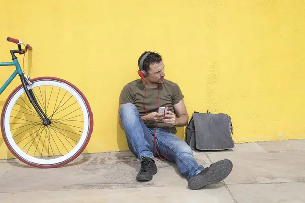 Man Casual Attire Red Headphones Sits Bright Yellow Wall Next Стокове Зображення