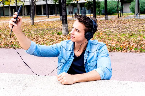 Young Male Denim Jacket Video Chats Using Headphones Holding Smartphone Royalty Free Φωτογραφίες Αρχείου