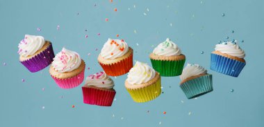 Banner with row of tumbling colorful rainbow cupcakes with falling sugar sprinkles