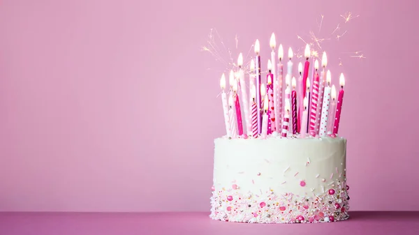 ピンクの誕生日ケーキともに多くのピンクの誕生日キャンドルとキラキラに対してピンクの背景にコピースペース — ストック写真