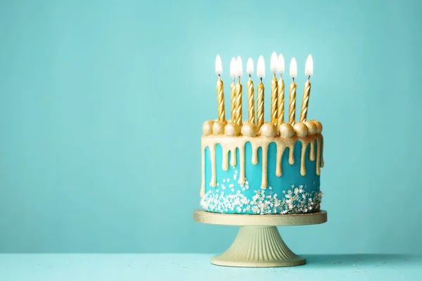トルコ石の背景に金の滴アイシングと金の誕生日キャンドルを持つエレガントなターコイズの誕生日ケーキ — ストック写真